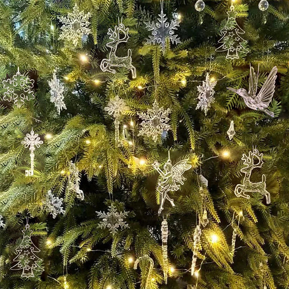 Clear acrylic snowflake, reindeer and bird ornaments on a lit Christmas tree