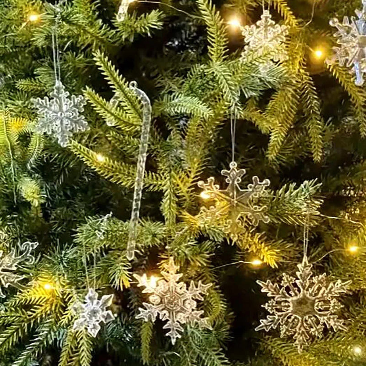 Clear acrylic snowflake and icicle ornaments hanging on a pine tree