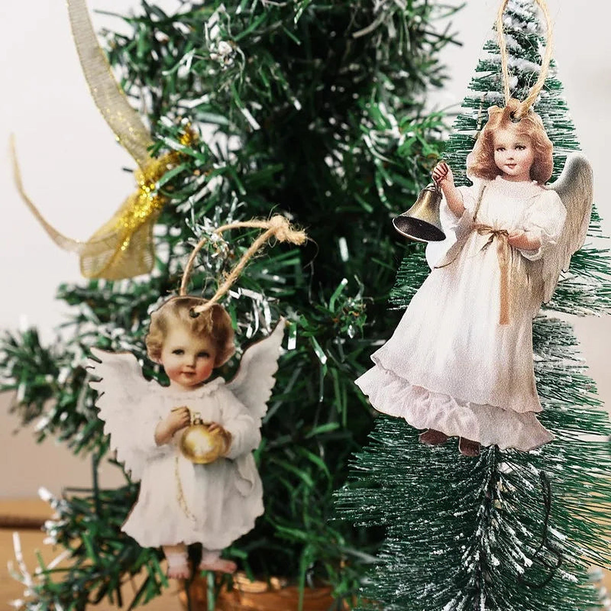Two wooden angel ornaments with bells hanging from twine