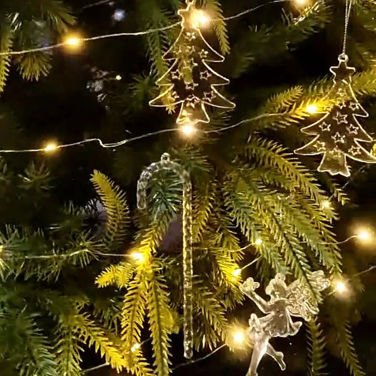 Clear acrylic Christmas tree, candy cane and fairy ornaments among warm lights