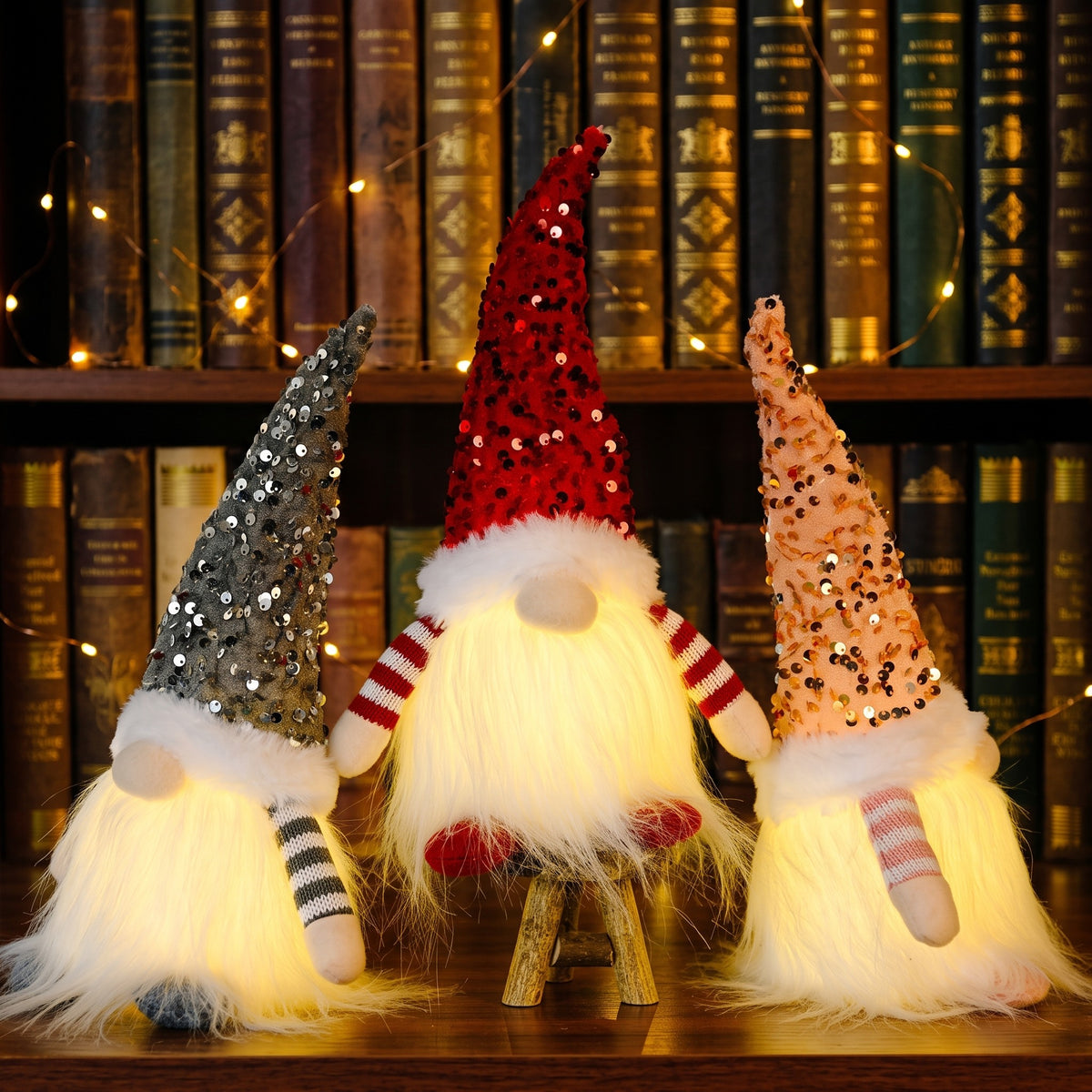 Light-up sequin gnomes in silver, red and champagne by a bookshelf
