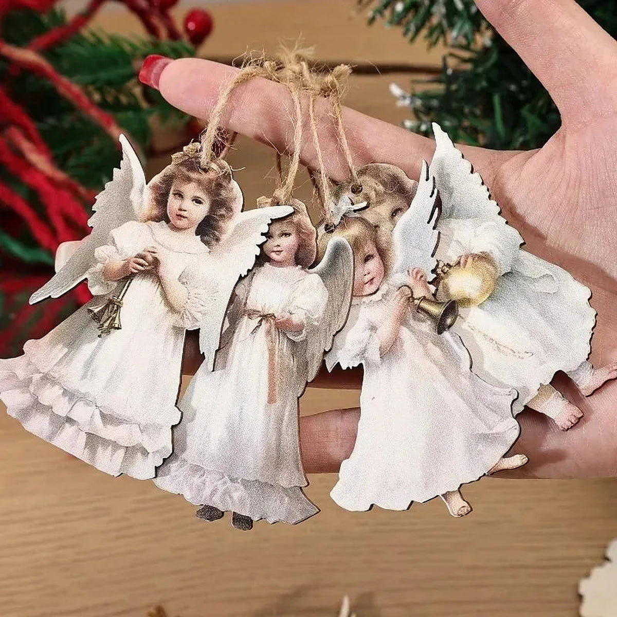 Hand holding four flat wooden angel ornaments with jute twine