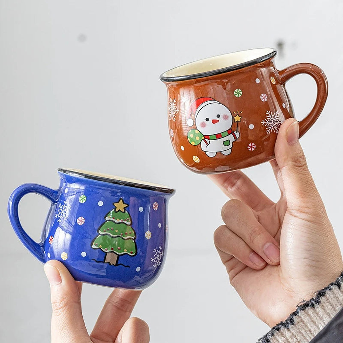 Blue Christmas tree and brown snowman mugs held in hands