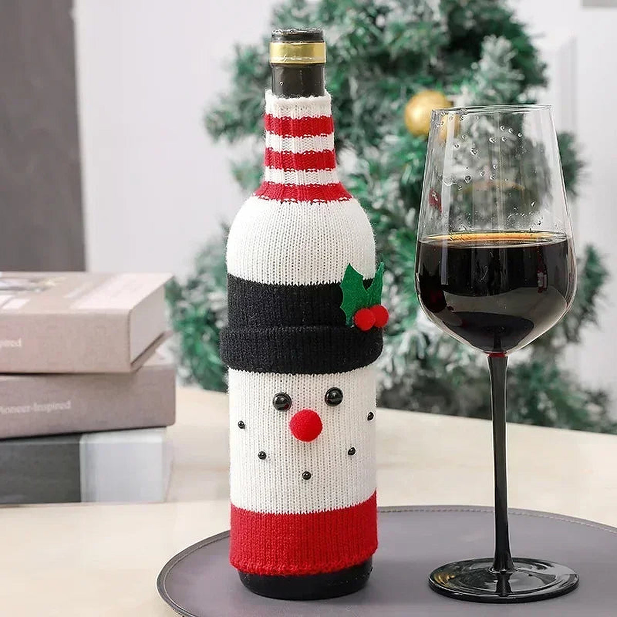 Snowman knit wine bottle cover beside a glass of wine
